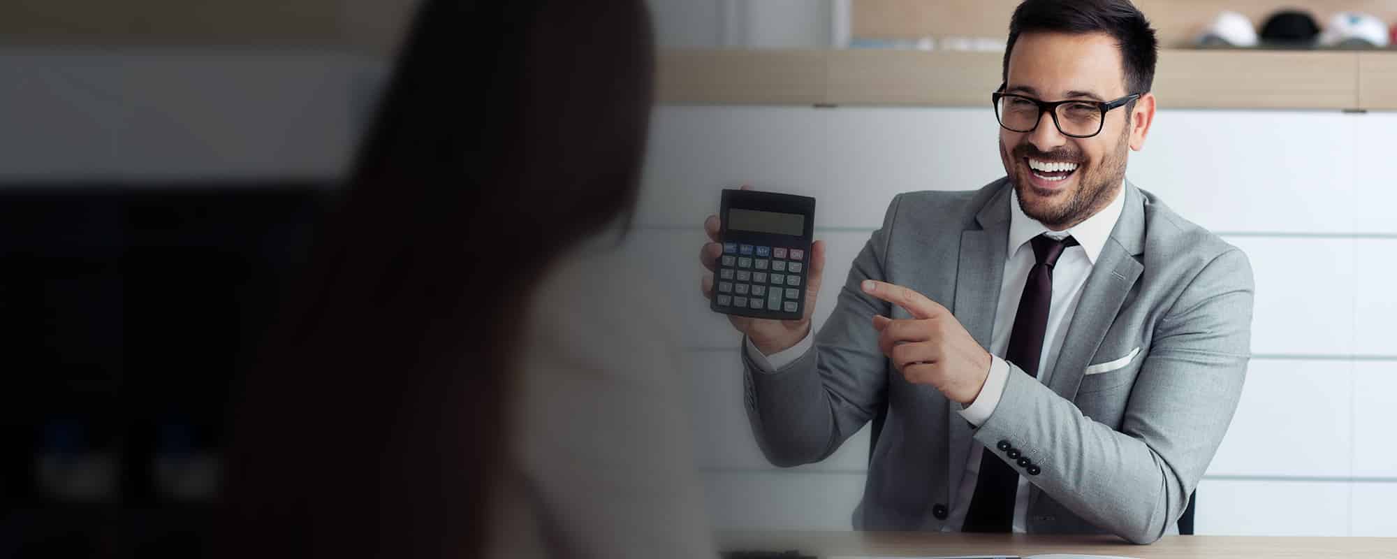 Smiling man in a gray suit holding a calculator, discussing financial options related to dealership reinsurance loans.