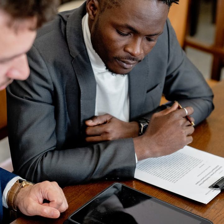 Two professionals discussing dealership profit strategies, one in a suit with a tablet and paperwork on a wooden table, emphasizing collaboration and financial analysis.